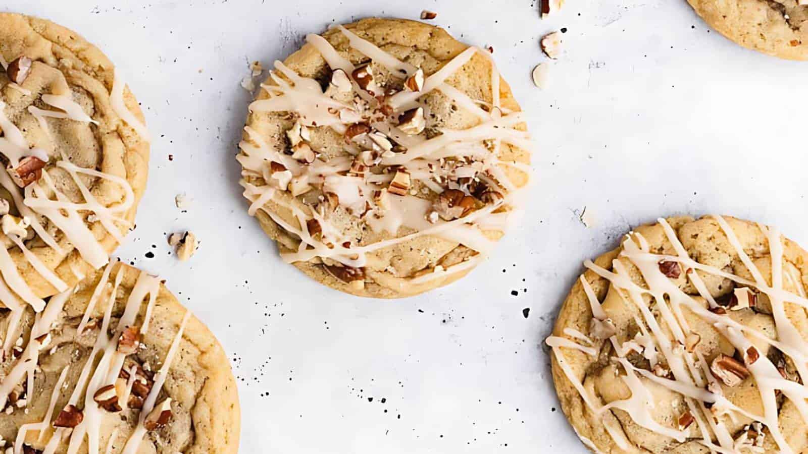 Cookies topped with chopped nuts and drizzled with icing are arranged on a white surface.
