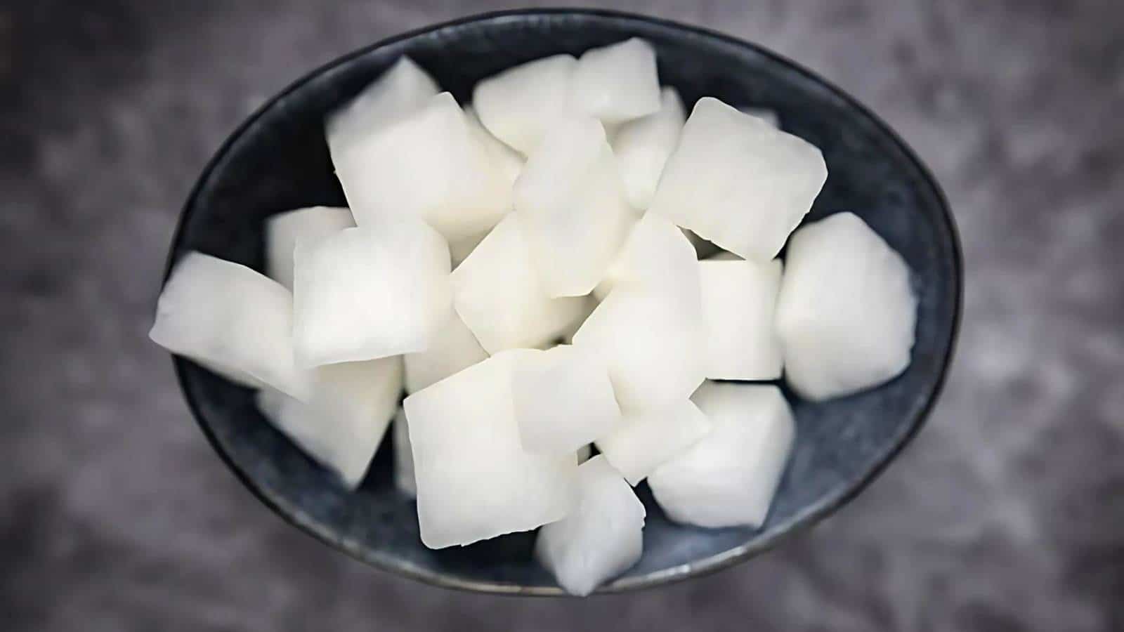A bowl filled with white, cubed pieces of daikon radish on a gray background.