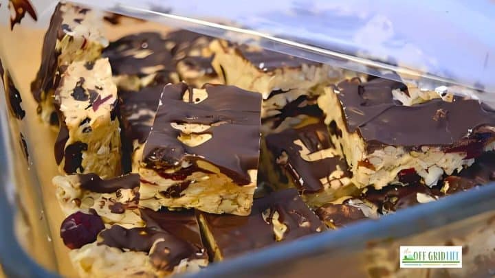 Glass container with homemade nougat bars topped with dark chocolate. Bars contain nuts and dried fruit pieces.