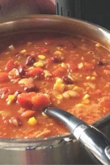 A metal pot filled with stovetop rice and beans sits on a stovetop with a ladle inside.