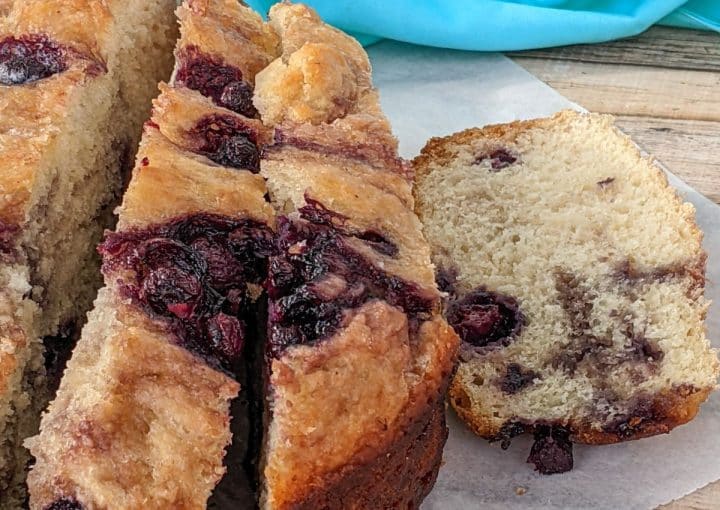 A sliced loaf of blueberry bread with visible blueberries and a light brown crust on a piece of parchment paper.