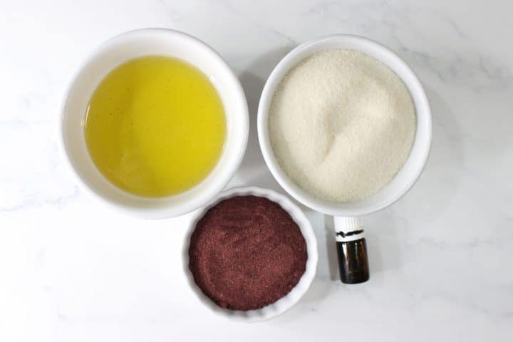 Three white bowls on a white surface, each containing a different ingredient: egg whites, granulated sugar, and a reddish-brown powder.