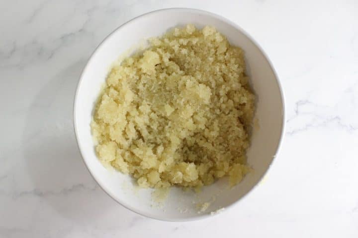 A white bowl filled with a coarse, pale yellow, grainy mixture sits on a white marble surface.