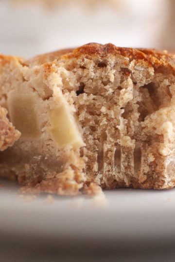 Close-up of a partially eaten slice of apple sour cream coffee cake with visible apple pieces, resting on a white plate with a fork holding a bite-sized piece.