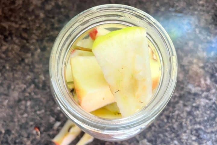 A glass jar filled with apple slices, viewed from above, sitting on a dark countertop.