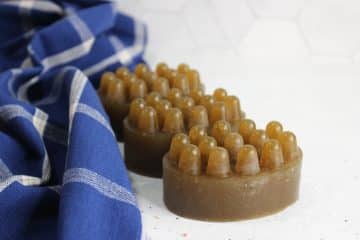 Two brown, oval-shaped massage soaps with raised bumps are placed on a white surface next to a blue and white checkered cloth, inspired by a soothing lemon soap recipe.