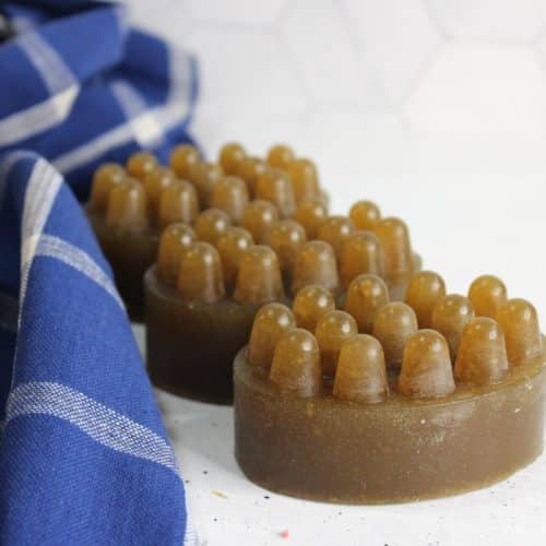 Two brown, oval-shaped massage soaps with raised bumps are placed on a white surface next to a blue and white checkered cloth, inspired by a soothing lemon soap recipe.
