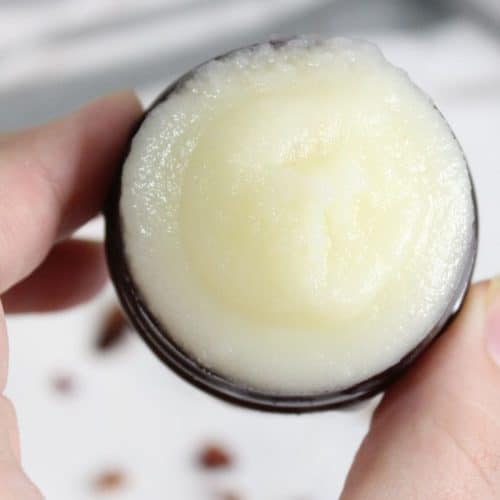 A hand holding an open container of solid, white beef tallow face cream balm.