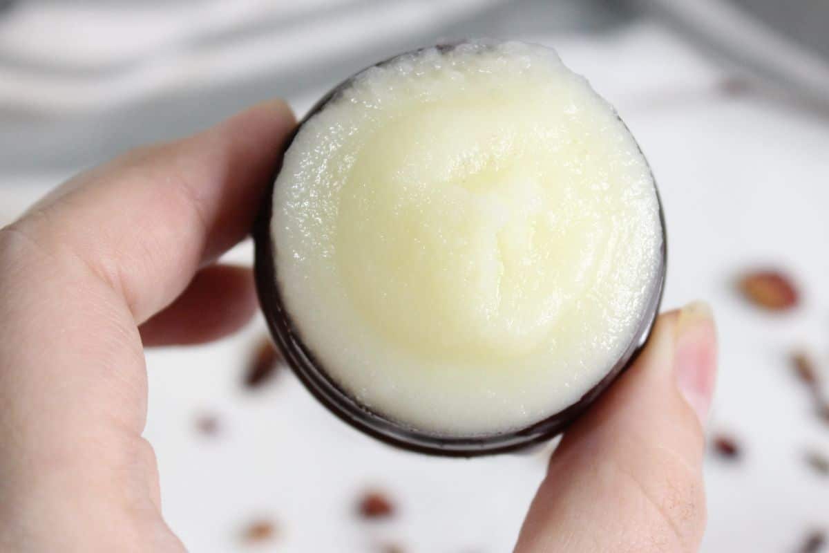 A hand holding an open container of solid, white beef tallow face cream balm.