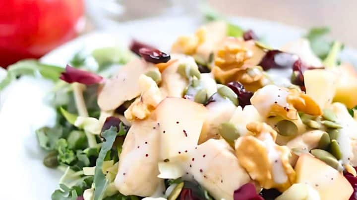 A close-up of a fresh salad with chopped apples, nuts, and seeds on a bed of leafy greens, drizzled with dressing.