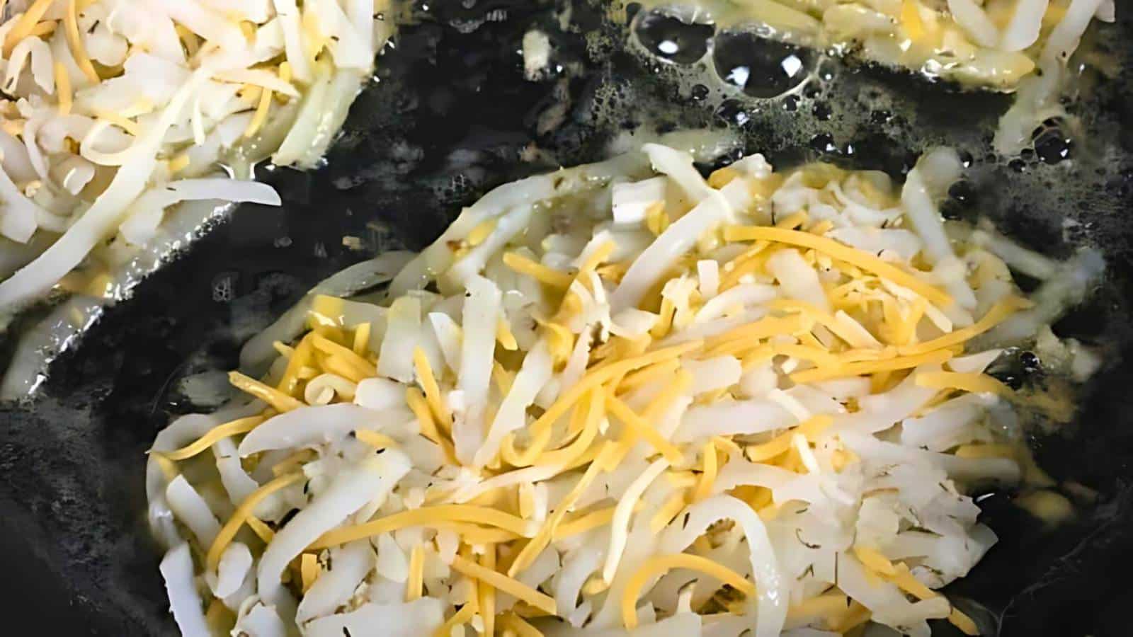 Shredded white and yellow cheese melting on a hot surface, with bubbling liquid surrounding it.