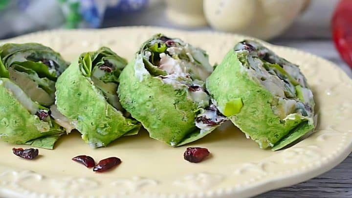 Sliced spinach wraps filled with chicken, leafy greens, and cranberries on a decorative plate.