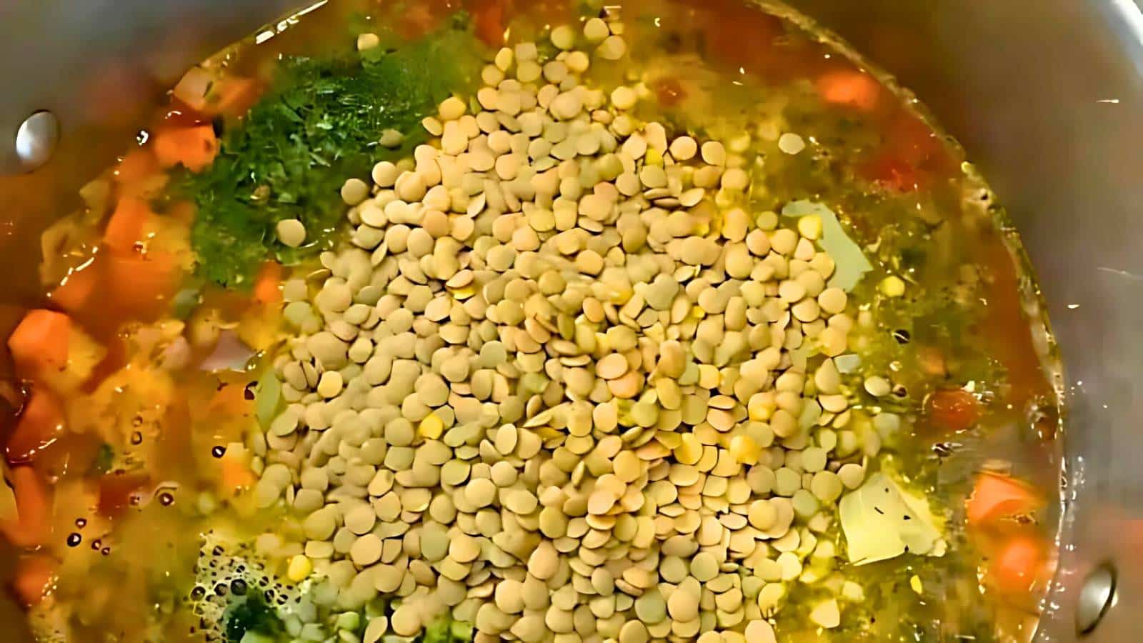 A pot filled with uncooked lentils, diced carrots, potatoes, and herbs in broth.