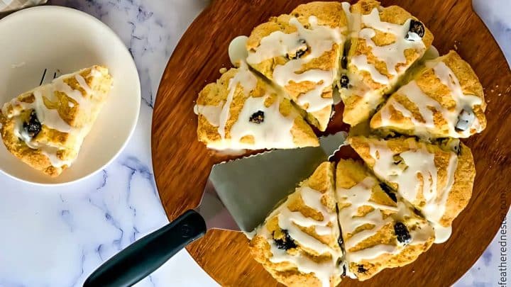 Eight lemon scones with icing on a wooden platter, one slice on a separate plate.