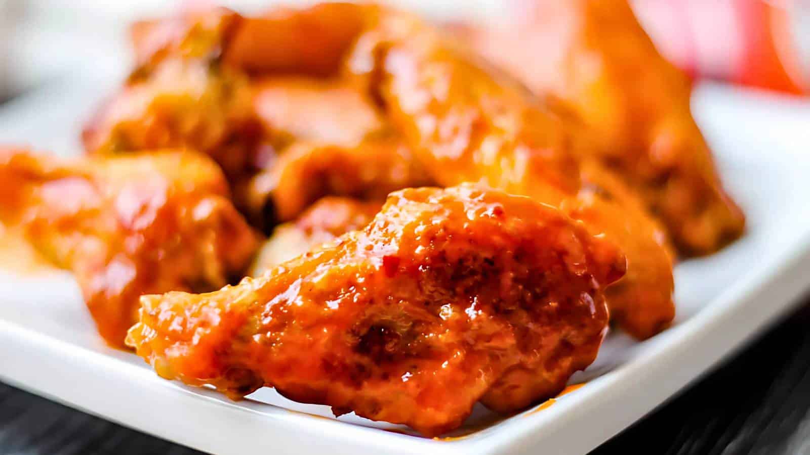 Close-up of saucy buffalo chicken wings on a white plate.