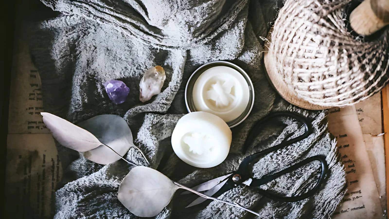 Crafting scene with scissors, twine, two crystals, a candle, and a cloth on a textured surface.