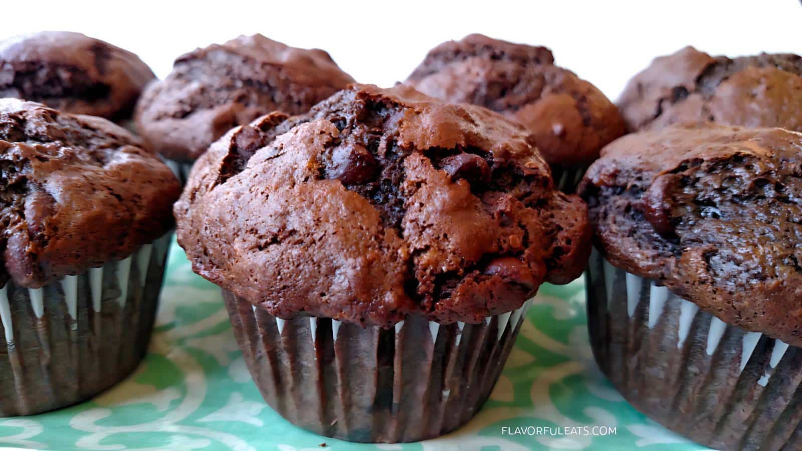 Close-up of six chocolate muffins on a green patterned surface.