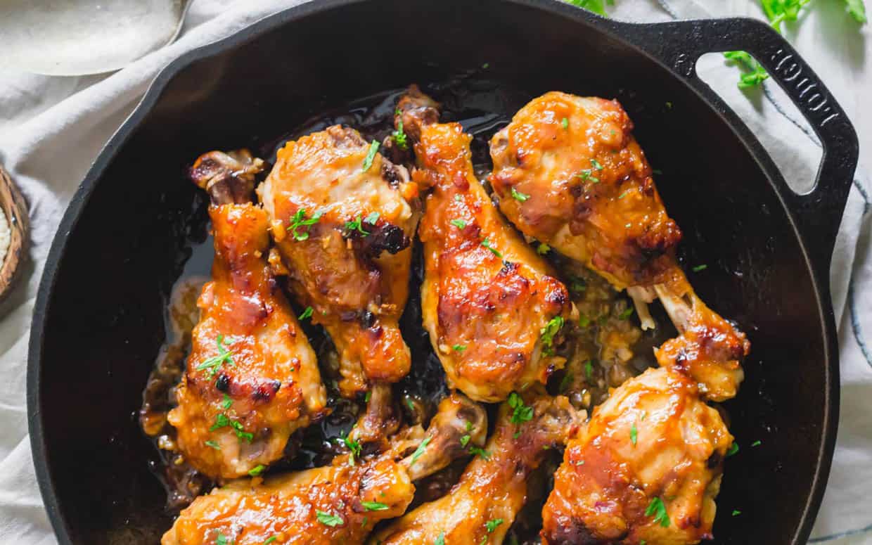 Cooked chicken drumsticks coated with seasoning are arranged in a black cast-iron skillet, garnished with chopped herbs.