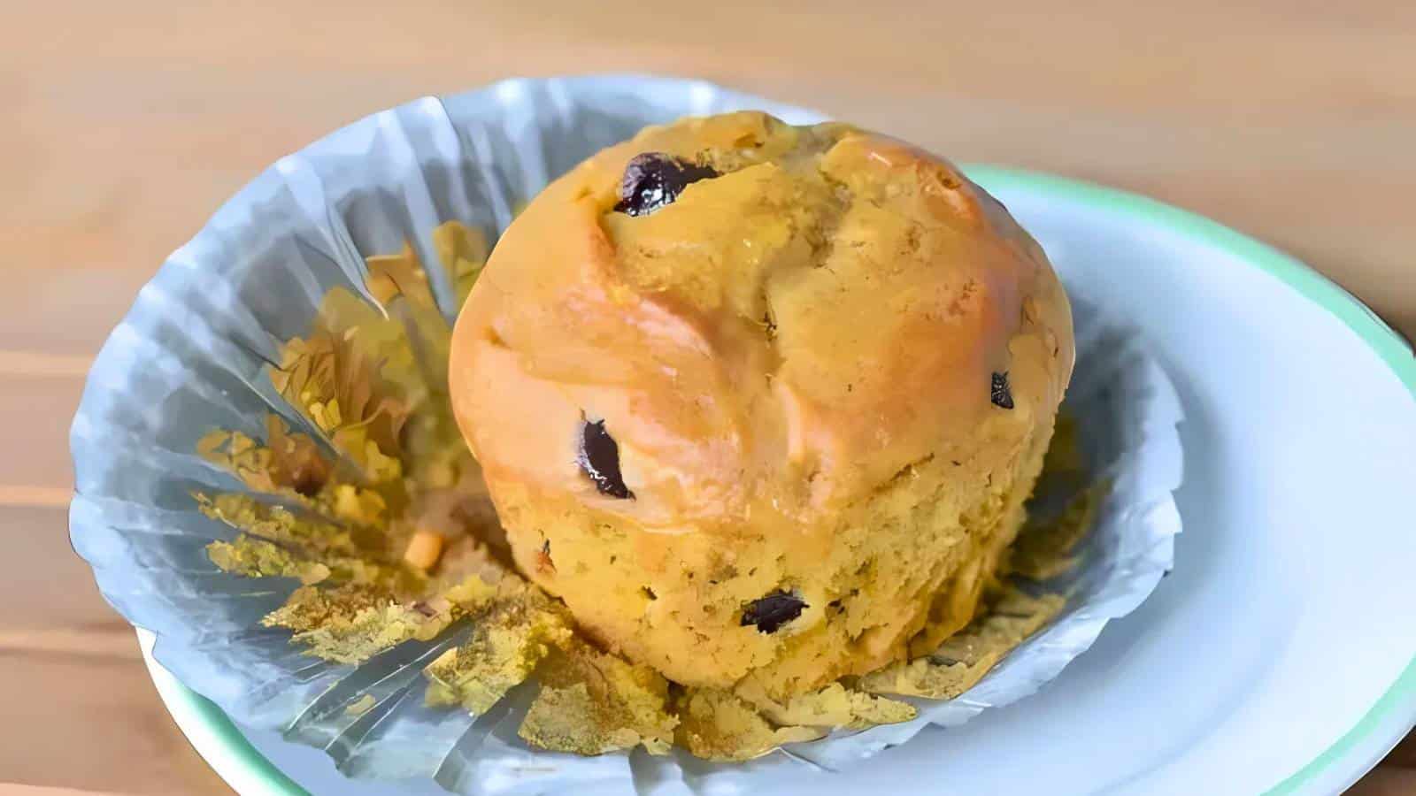 A muffin with chocolate chips sits in a metallic baking cup on a ceramic plate.