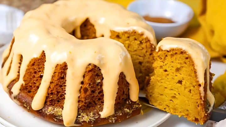A glazed bundt cake with a slice cut out, revealing a moist, golden interior.