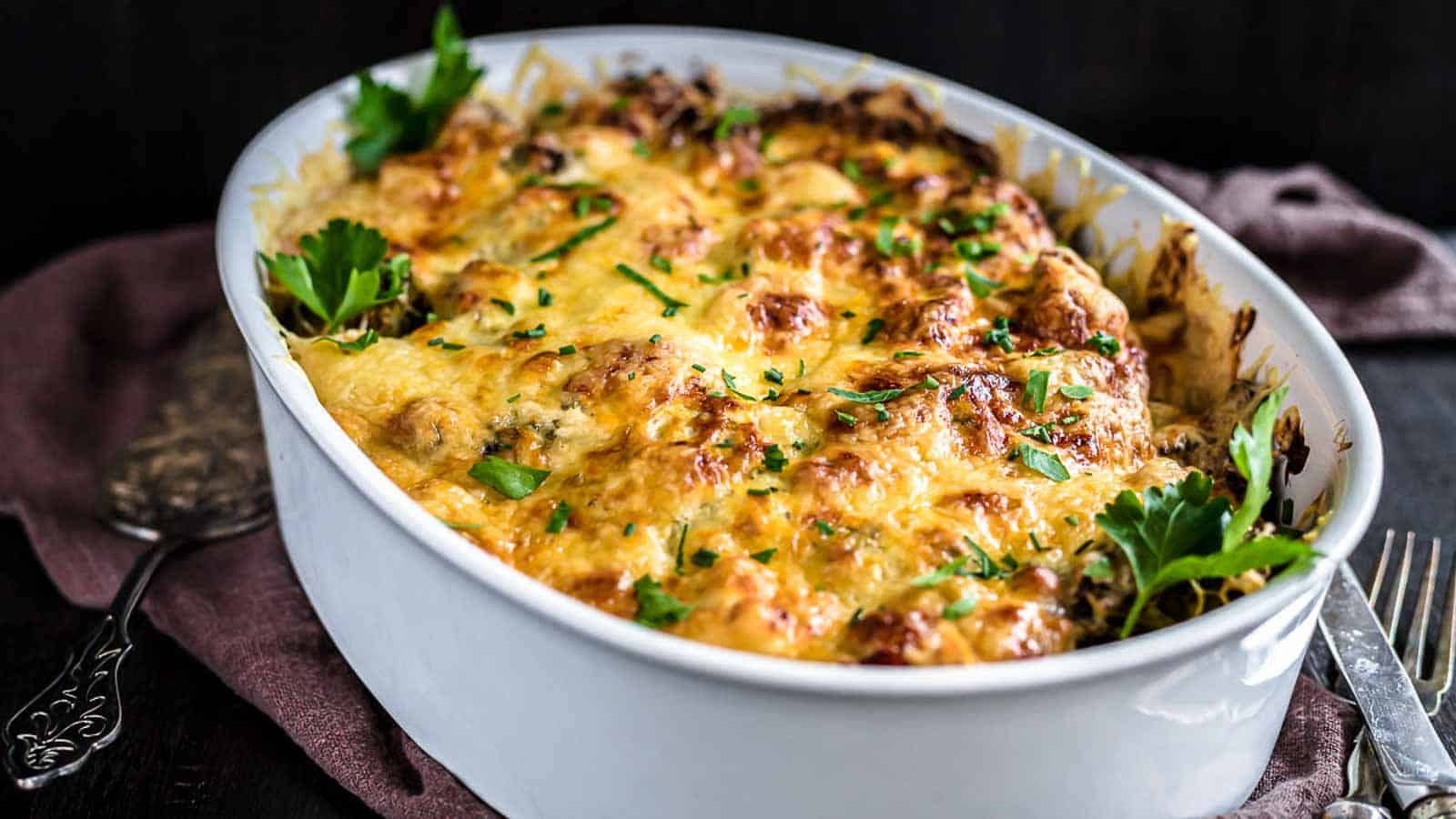 Baked casserole topped with melted cheese and garnished with parsley in an oval dish.