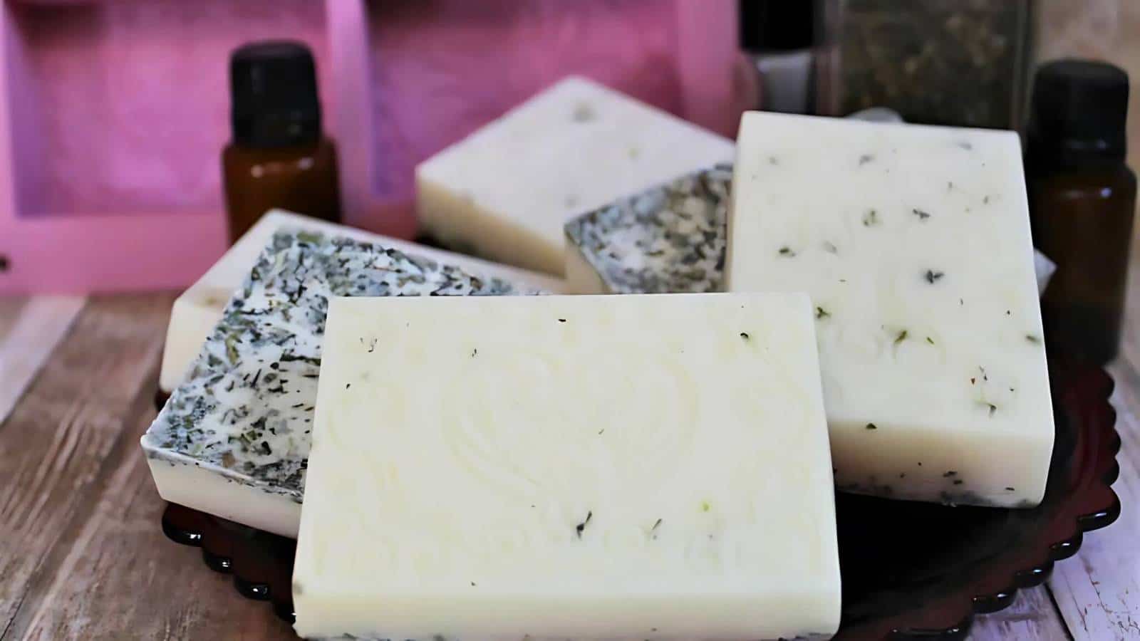 A plate with rectangular bars of white and speckled soap, surrounded by small brown bottles, set on a wooden surface.