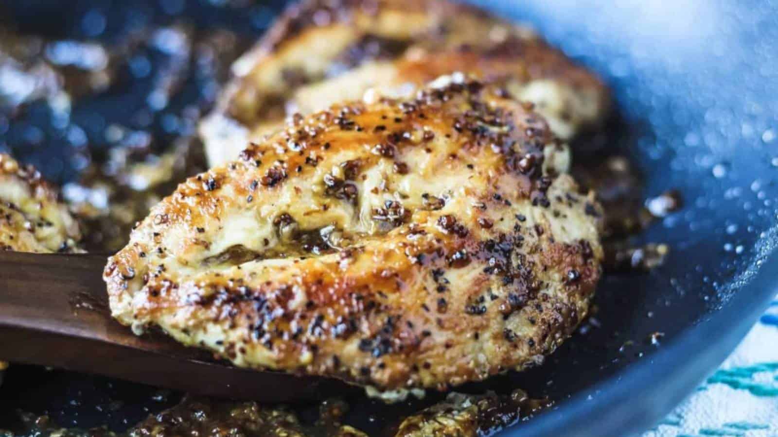 Seasoned chicken breasts cooking in a black skillet with visible herbs and a golden-brown crust.