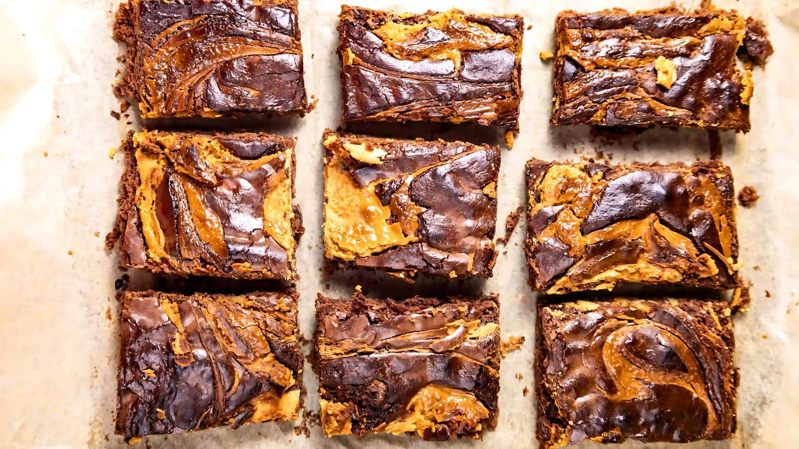 Nine chocolate brownies with swirled peanut butter on parchment paper.