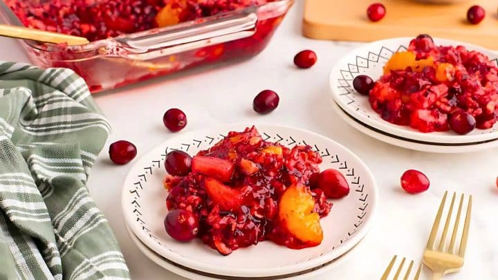 Two plates with cranberry-orange dessert on a table with a green cloth. A baking dish with more dessert and scattered cranberries are in the background.