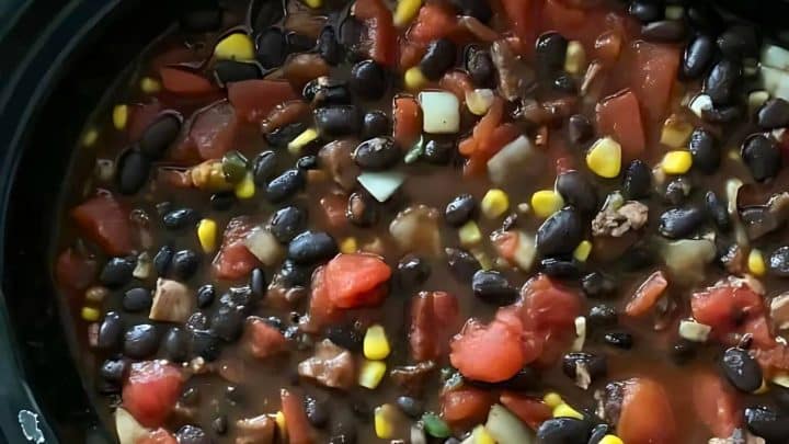A close-up of a hearty stew containing black beans, corn, diced tomatoes, and various vegetables in a thick broth.