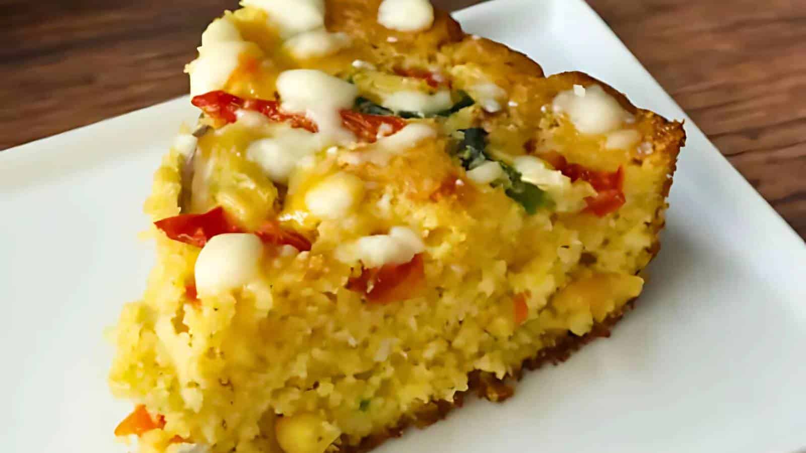 A slice of savory cornbread with visible corn kernels, red bell peppers, and melted cheese on a white plate.