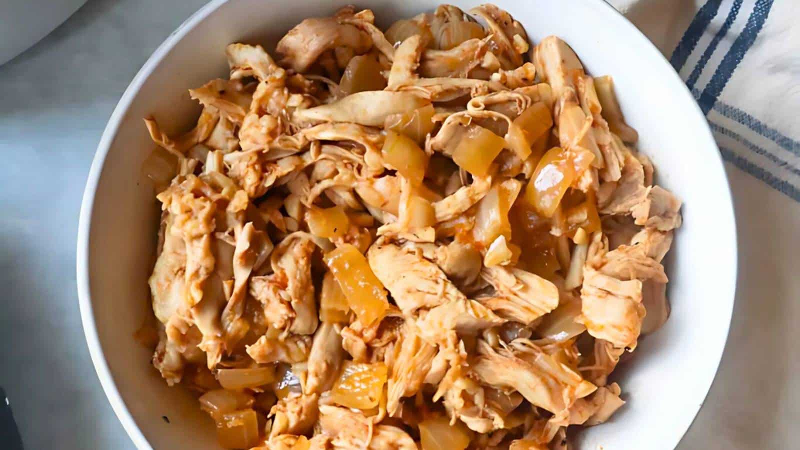 Bowl of shredded chicken mixed with sautéed onions in a light sauce.