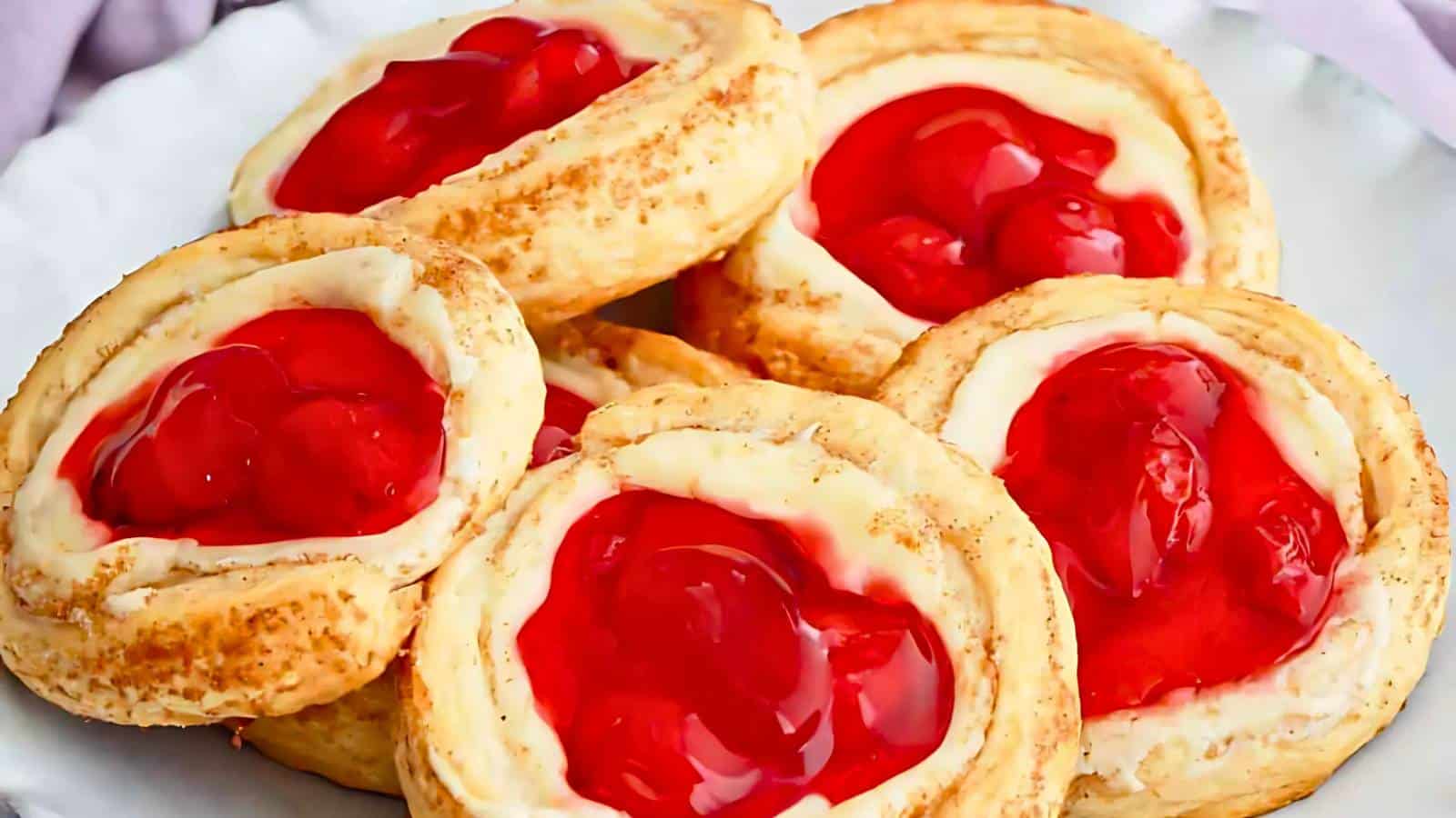 A plate of cherry-topped pastries with flaky crusts and cream cheese filling.