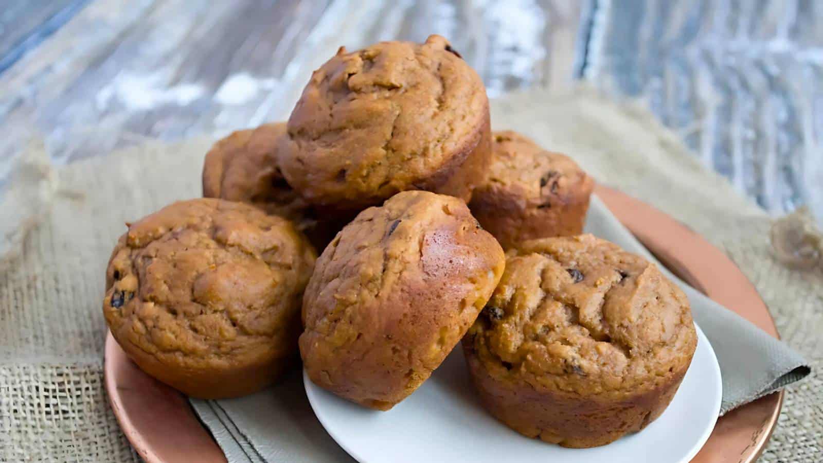 A plate of six pumpkin muffins stacked on a burlap cloth.