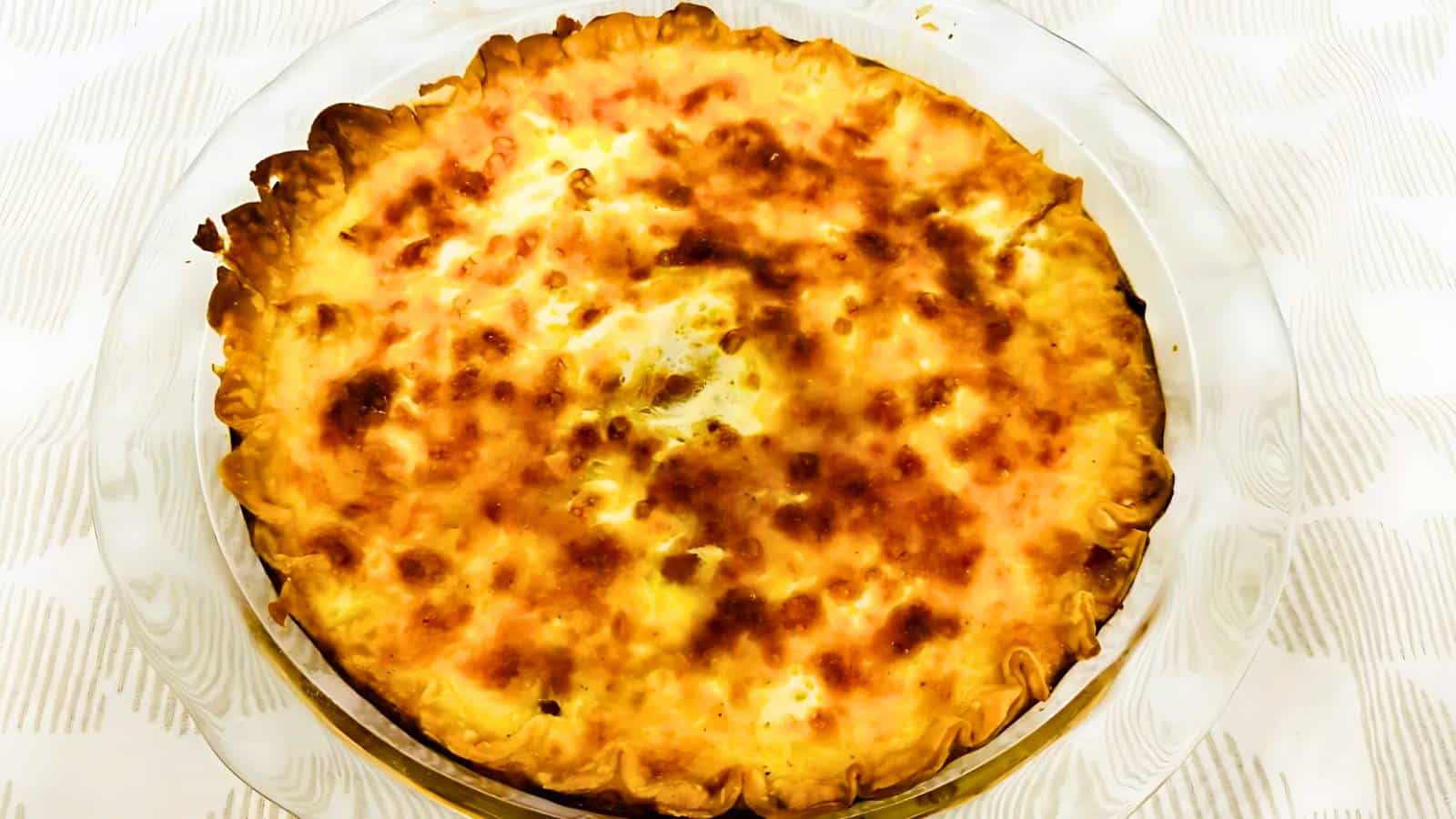 A freshly baked quiche with a golden-brown crust placed on a clear glass plate.