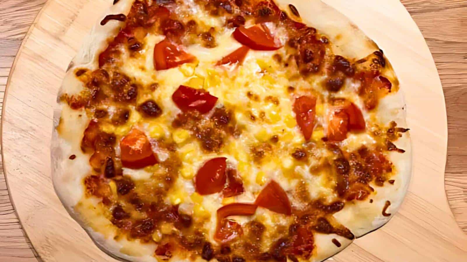 A pizza with melted cheese, tomato chunks, and browned edges on a wooden surface.