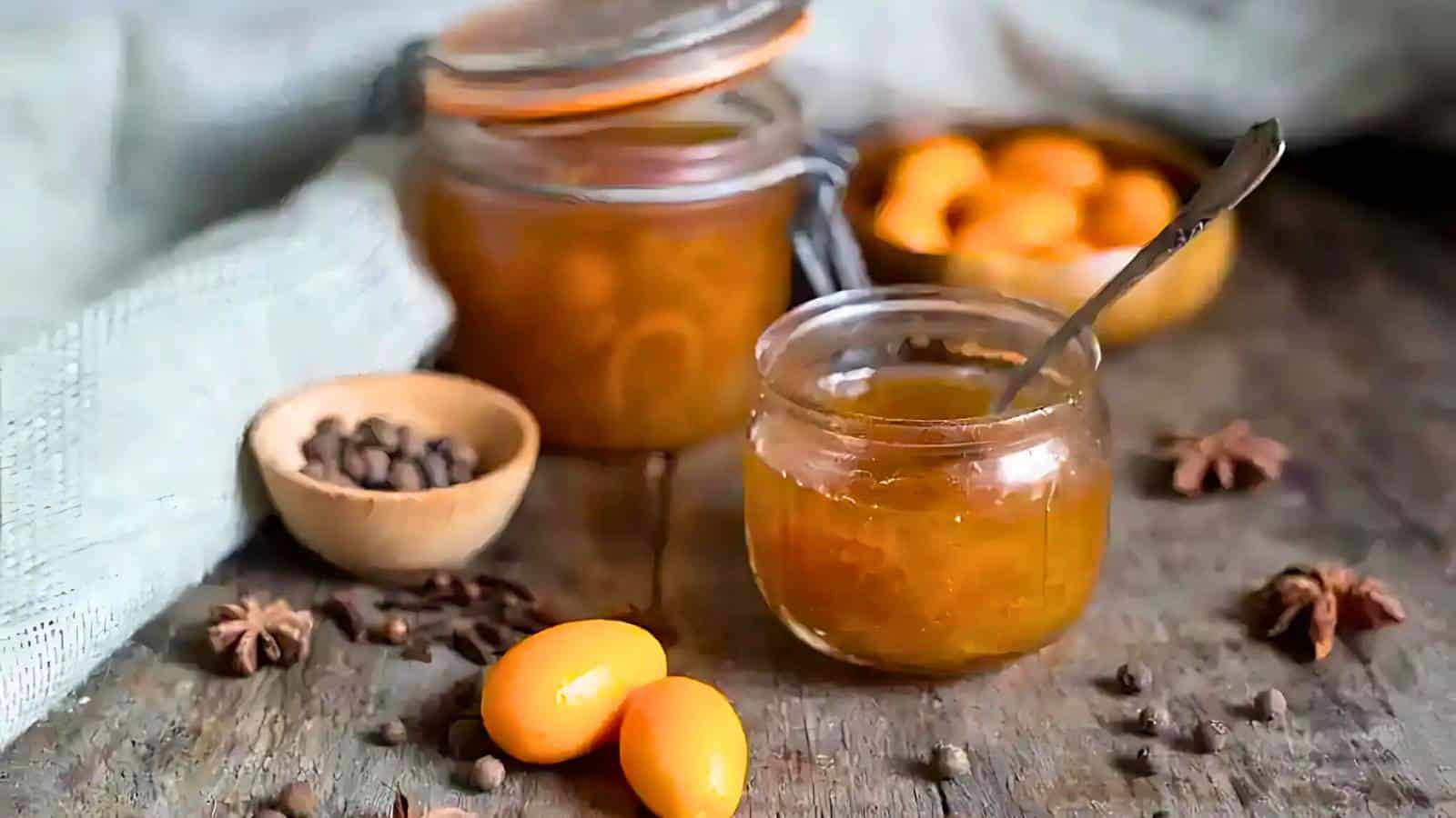 A plate with a jar of persimmon jam, a whole persimmon fruit, and a slice of rustic bread.