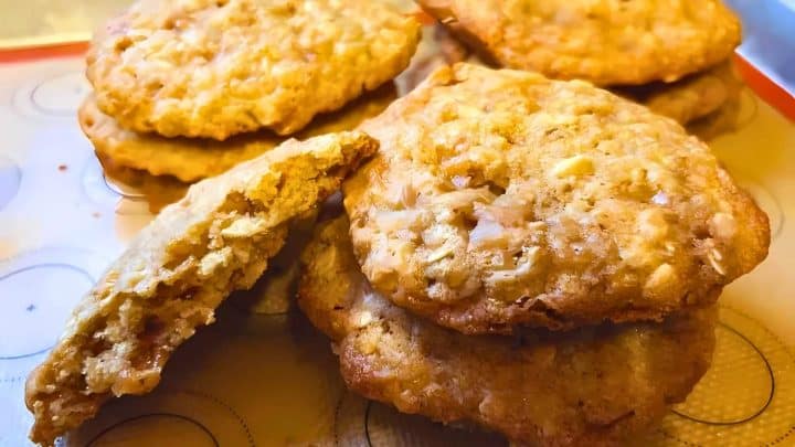 A batch of oatmeal cookies, some stacked and one partially broken, on a baking sheet.