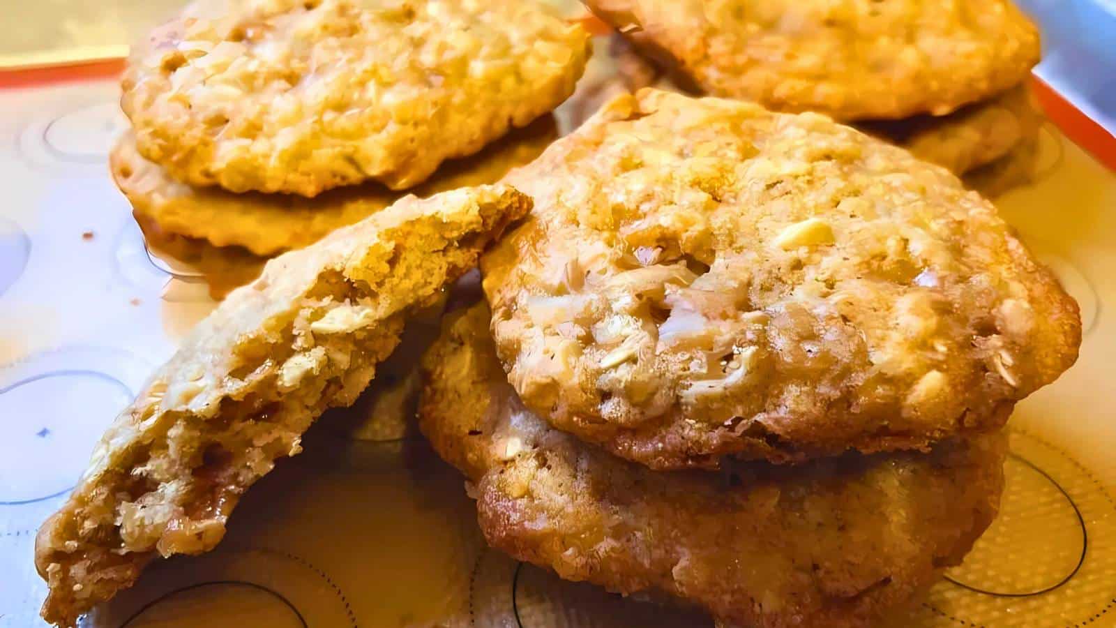 A batch of oatmeal cookies, some stacked and one partially broken, on a baking sheet.