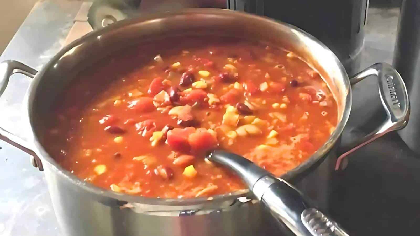 A pot of vegetable soup with beans, corn, and diced tomatoes, sitting on a stove with a ladle.