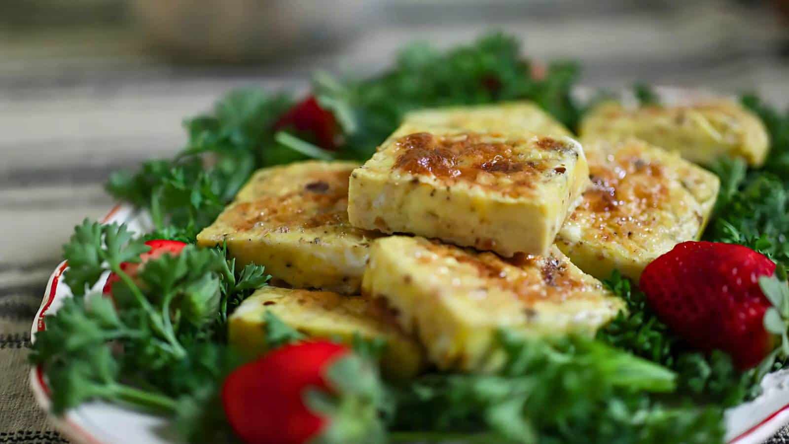 A plate of browned square-shaped egg pieces is garnished with fresh parsley and strawberries.
