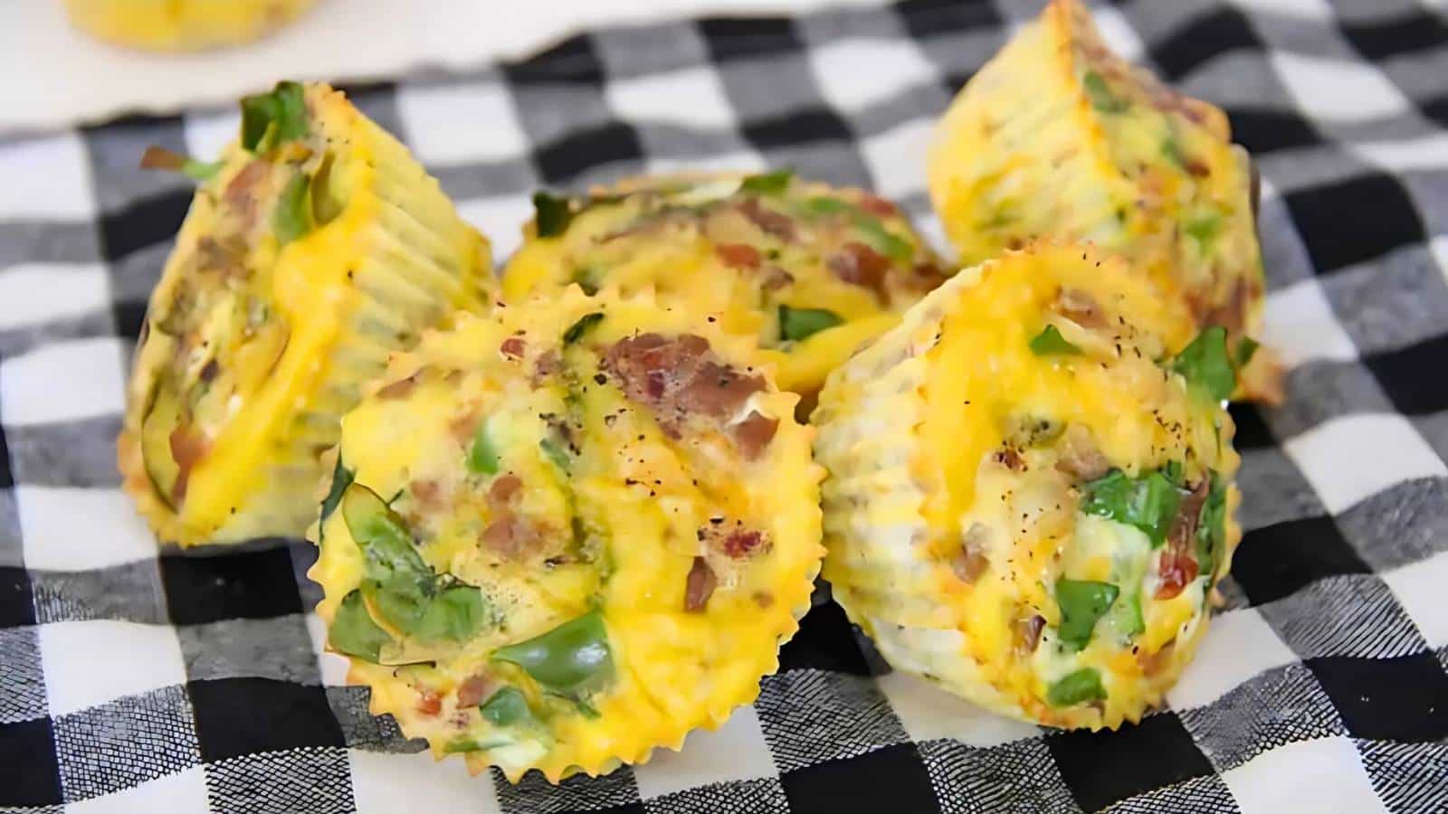 Five egg muffins with spinach and bacon on a black and white checkered cloth.