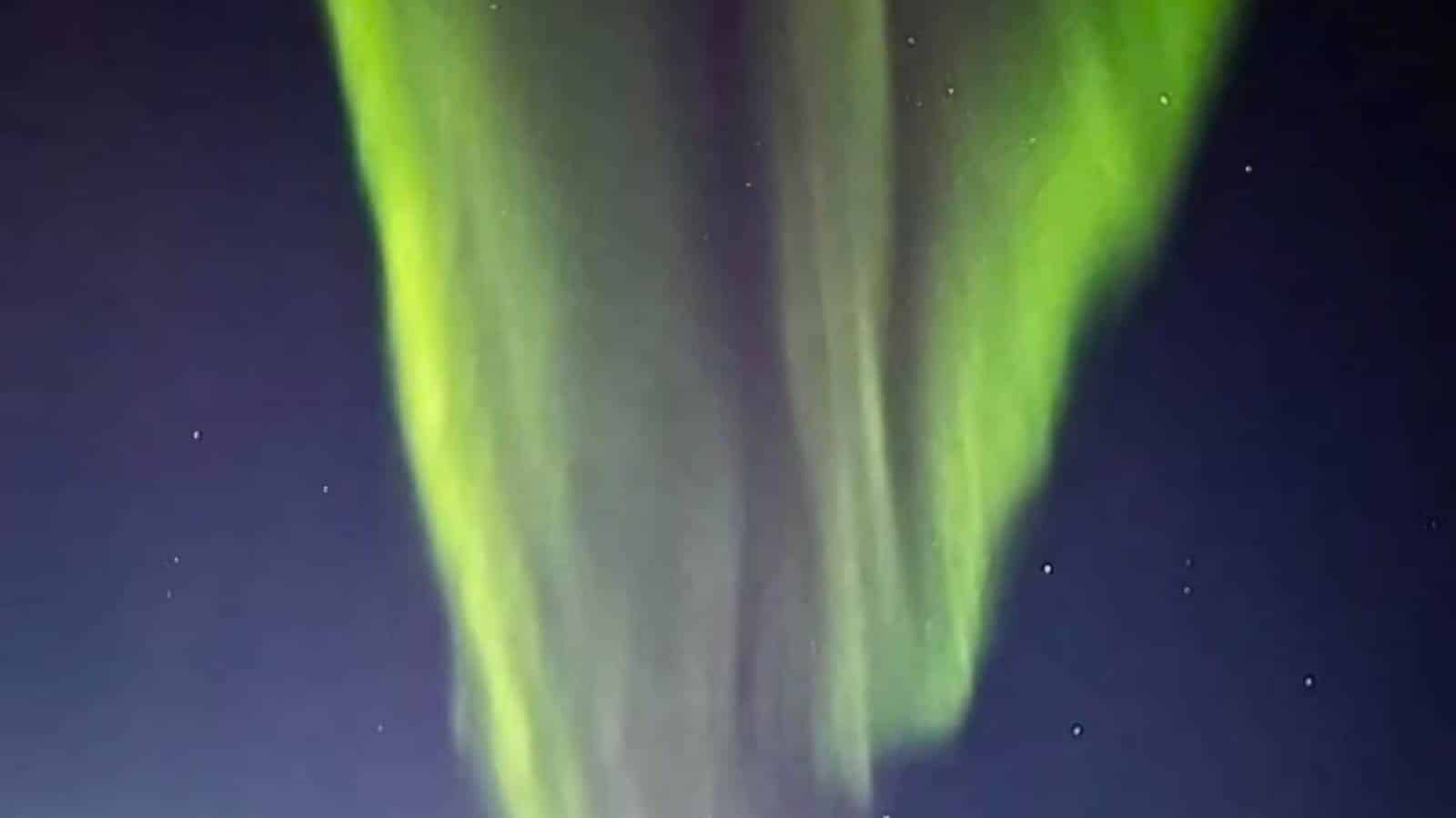 Vertical display of green aurora lights against a dark, starry sky.