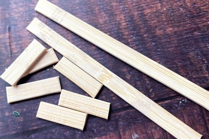 Several rectangular wooden pieces, including two longer strips and several shorter segments, are spread out on a dark wooden surface.