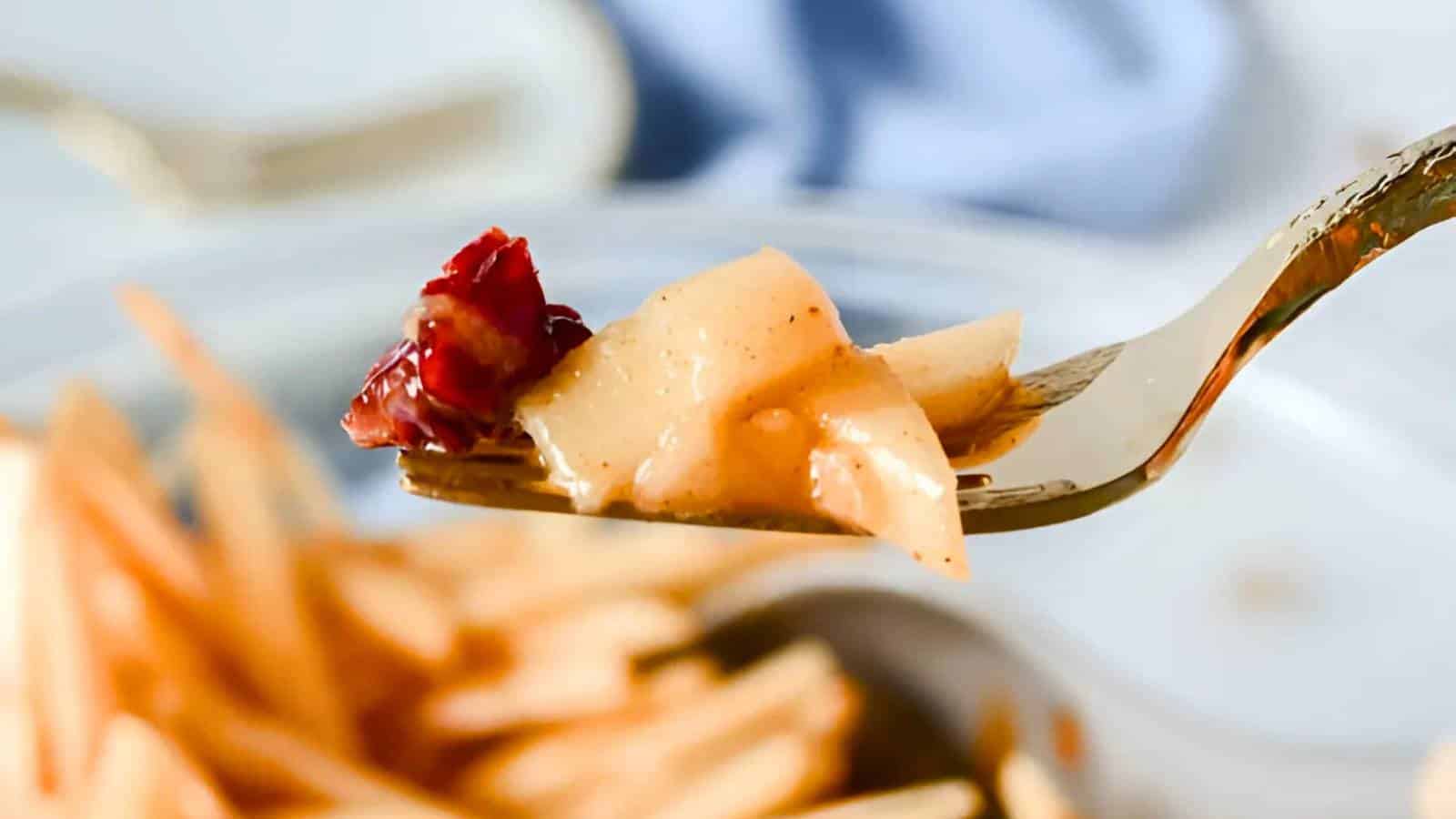 A fork holding a piece of apple topped with cranberries and sauce, with a blurred dish of apple slices in the background.