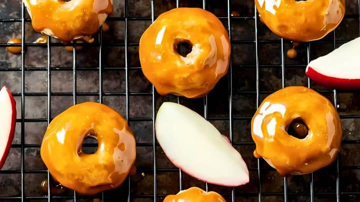 Small donuts with caramel glaze on a cooling rack, accompanied by apple slices.