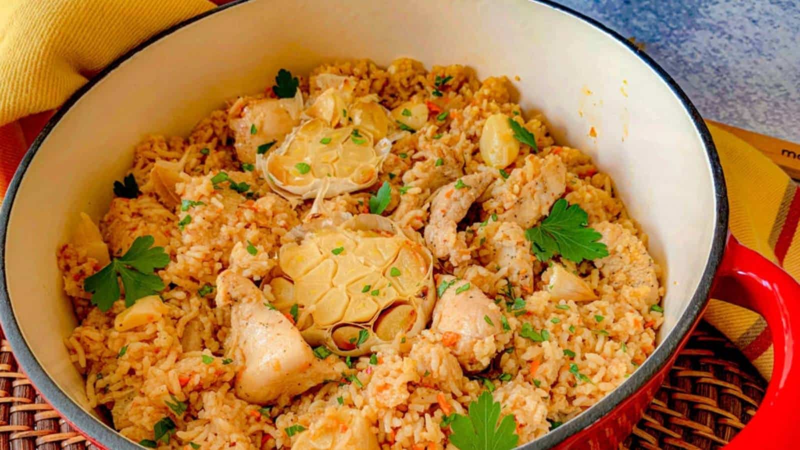 A pot of chicken and rice topped with parsley and halved garlic.