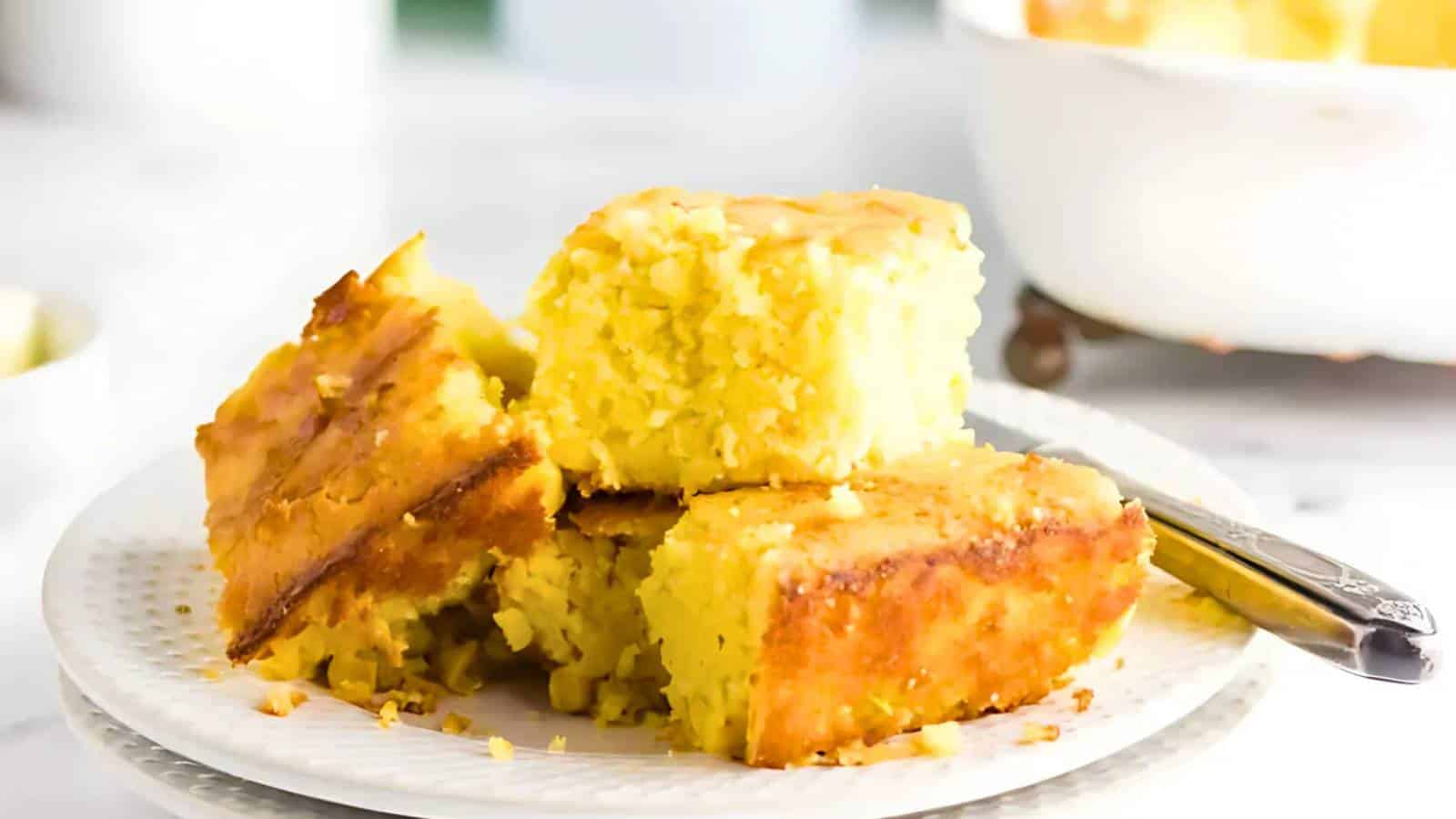 A plate with three pieces of cornbread and a fork, placed on a white surface.