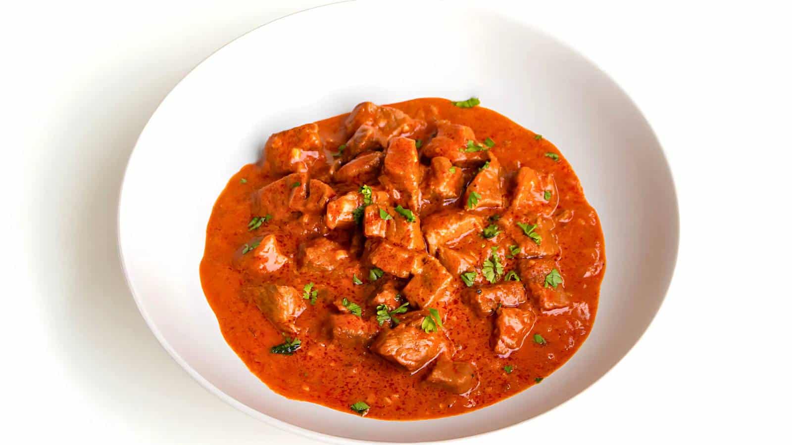 A white bowl filled with chunks of meat in a thick, red curry sauce, garnished with fresh cilantro.