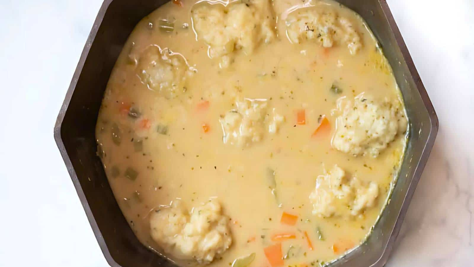 A pot of soup with dumplings, carrots, celery, and herbs in a creamy broth.